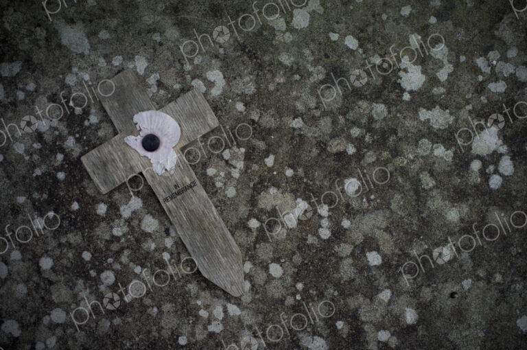 A small wooden cross with a poppy symbol commemorating the wartime dead, on a stone.