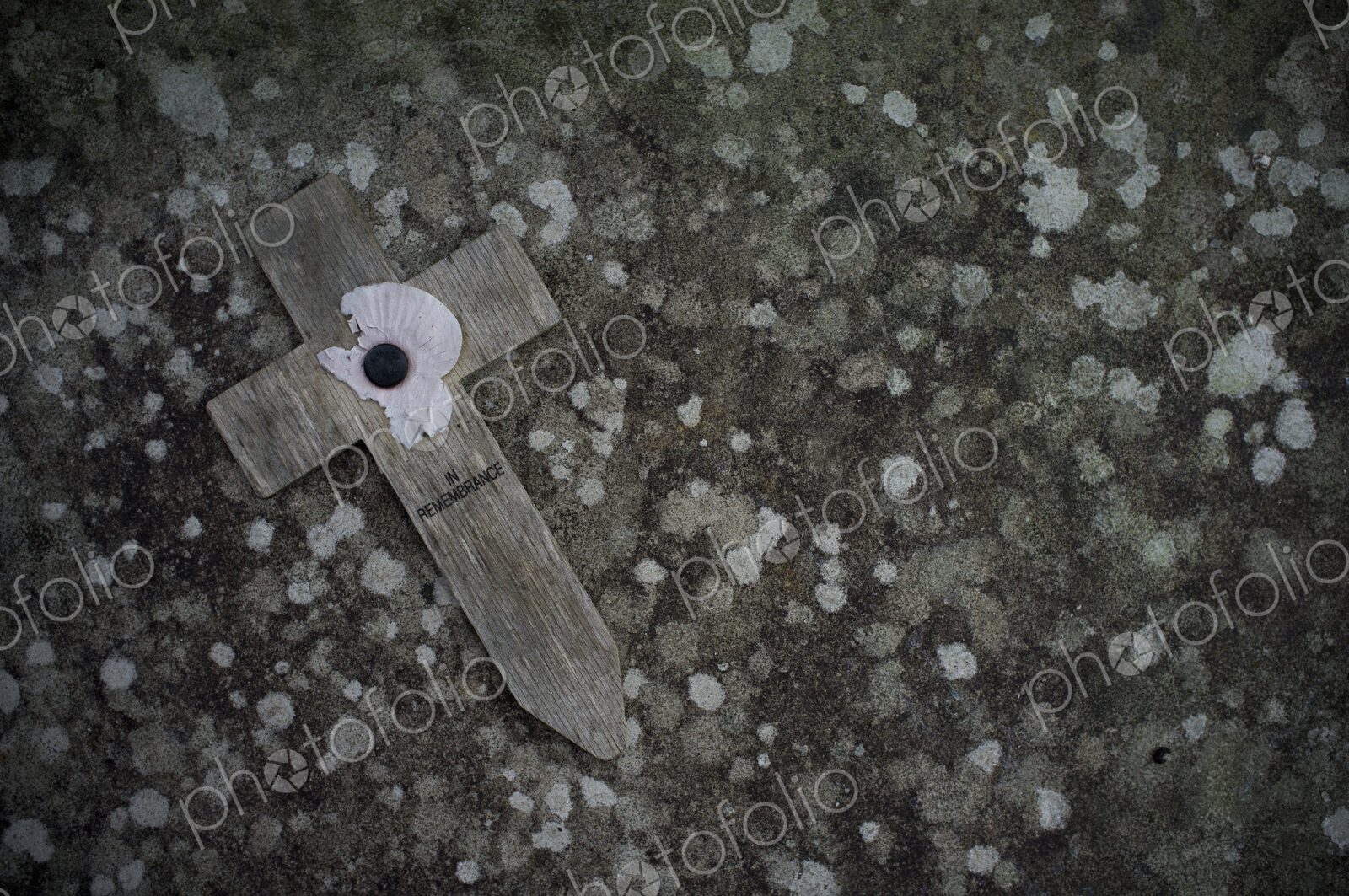 A small wooden cross with a poppy symbol commemorating the wartime dead, on a stone.