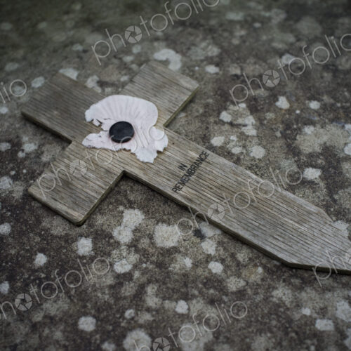 A small wooden cross with a poppy symbol commemorating the wartime dead, on a stone. A small wooden cross with a poppy symbol commemorating the wartime dead, on a stone.