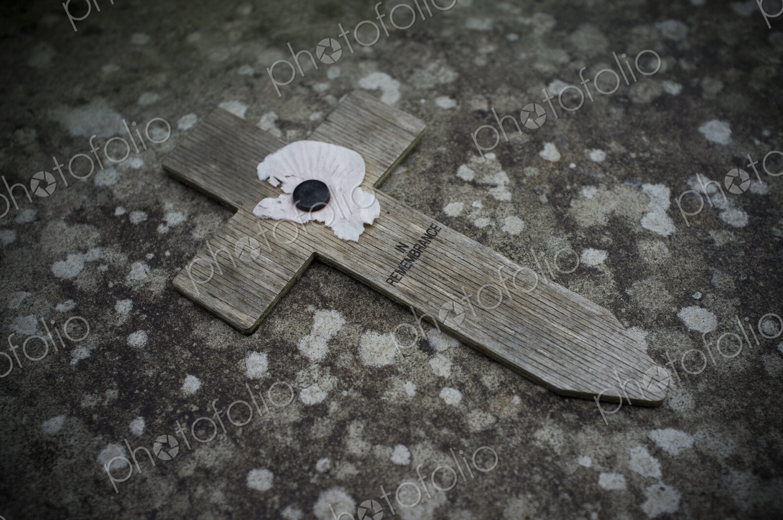 A small wooden cross with a poppy symbol commemorating the wartime dead, on a stone.