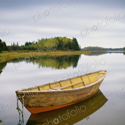 A small wooden dory or rowing boat moored on flat calm water, in Savage harbor on… A small wooden dory or rowing boat moored on flat calm water, in Savage harbor on…