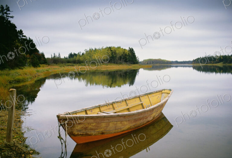 A small wooden dory or rowing boat moored on flat calm water, in Savage harbor on…