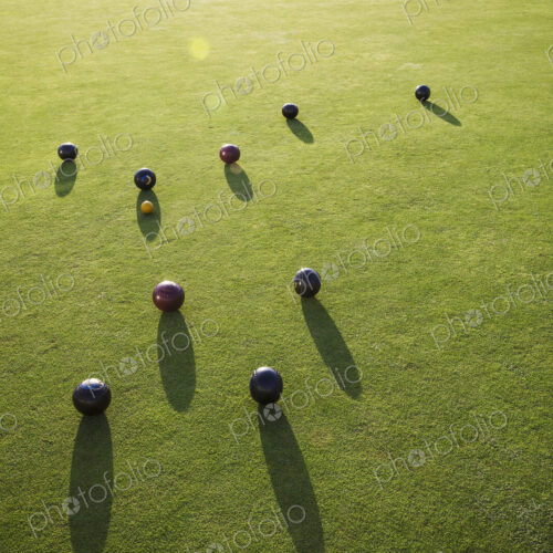 A small yellow target jack ball and a cluster of lawn bowls around it. People in the… A small yellow target jack ball and a cluster of lawn bowls around it. People in the…