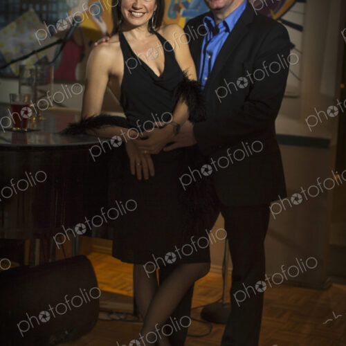 A smartly dressed man and woman side by side by a piano.