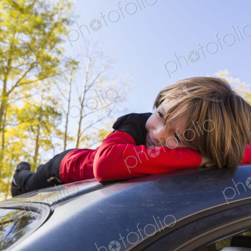 A smiling 6 year old boy lying on the hood of a blue SUV in woodland. A smiling 6 year old boy lying on the hood of a blue SUV in woodland.