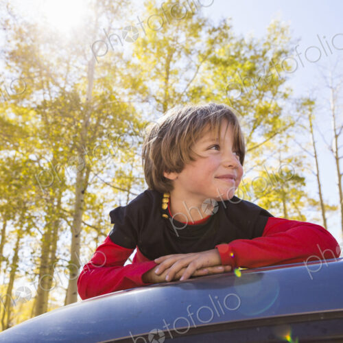 A smiling 6 year old boy lying on the hood of a blue SUV in woodland. A smiling 6 year old boy lying on the hood of a blue SUV in woodland.
