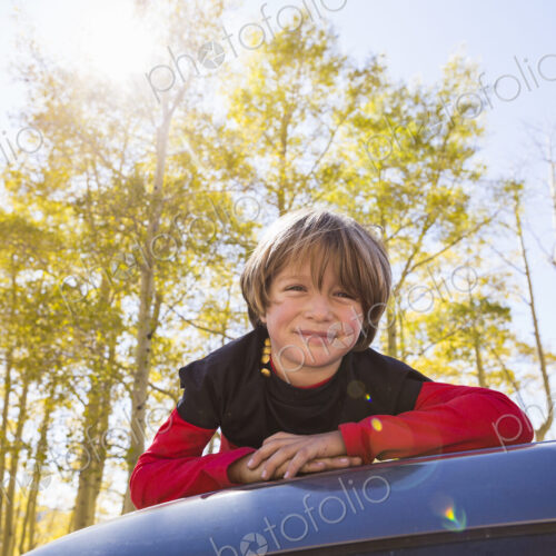 A smiling 6 year old boy lying on the hood of a blue SUV in woodland. A smiling 6 year old boy lying on the hood of a blue SUV in woodland.