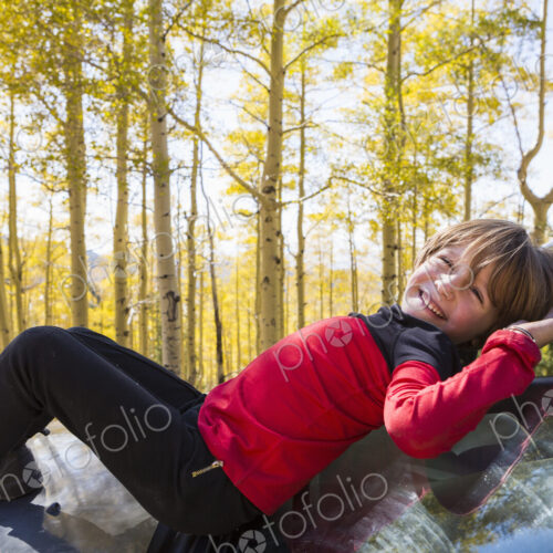 A smiling 6 year old boy lying on the hood of a blue SUV in woodland. A smiling 6 year old boy lying on the hood of a blue SUV in woodland.