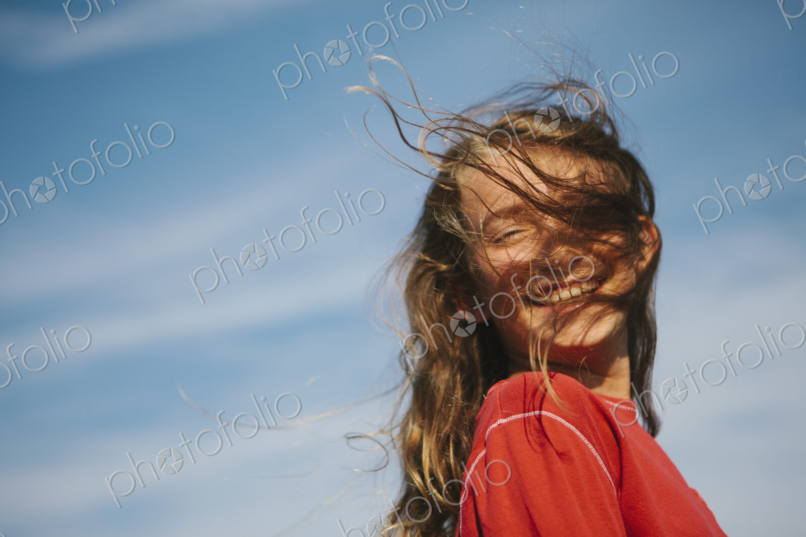 A smiling nine year old girl, with the wind blowing her hair over her face.