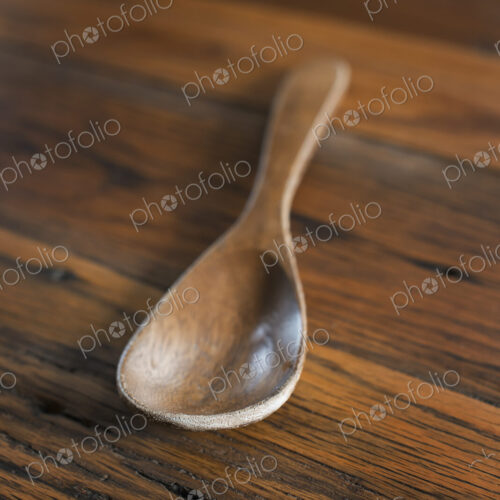 A smooth polished wooden ladle or spoon on a grained wooden tabletop. A smooth polished wooden ladle or spoon on a grained wooden tabletop.