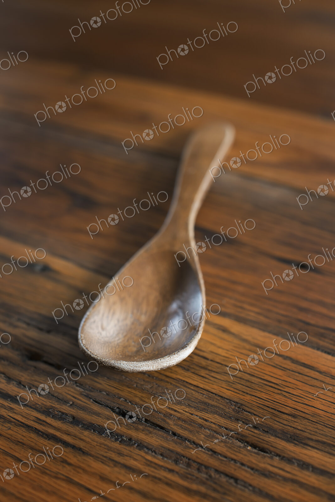 A smooth polished wooden ladle or spoon on a grained wooden tabletop.