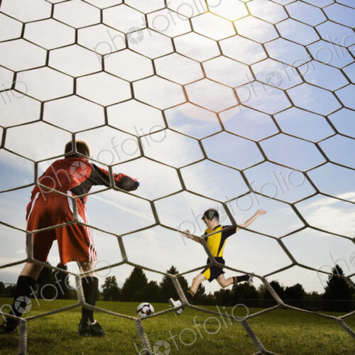 A soccer player taking aim and kicking at the goal, view from behind the goal keeper. A soccer player taking aim and kicking at the goal, view from behind the goal keeper.