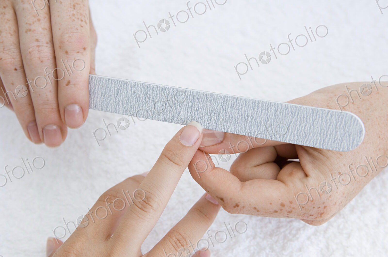 A spa treatment centre. A young woman having a manicure, having her fingernail filed.