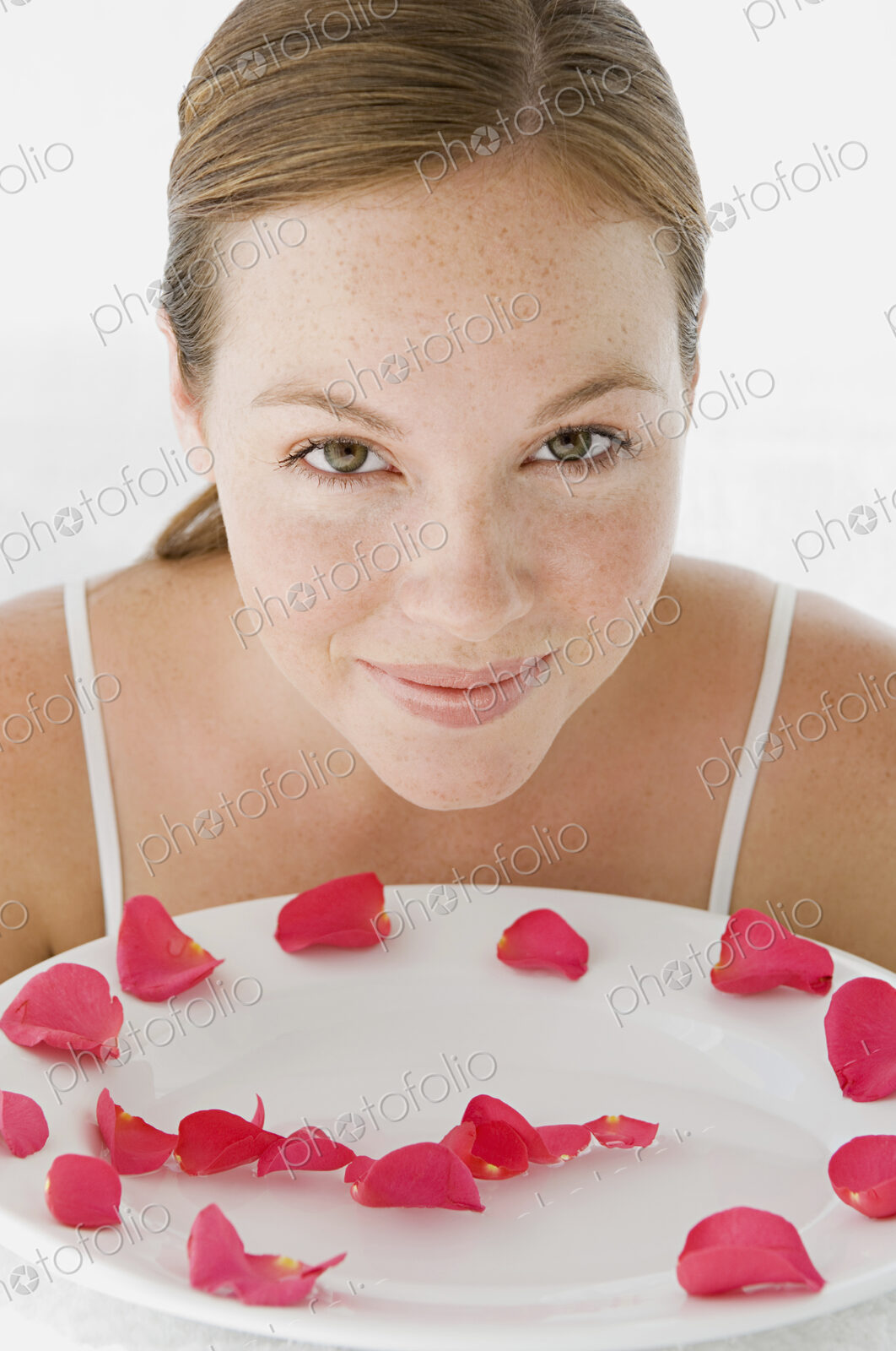 A spa treatment centre. A young woman with a white dish of pink rose petals.