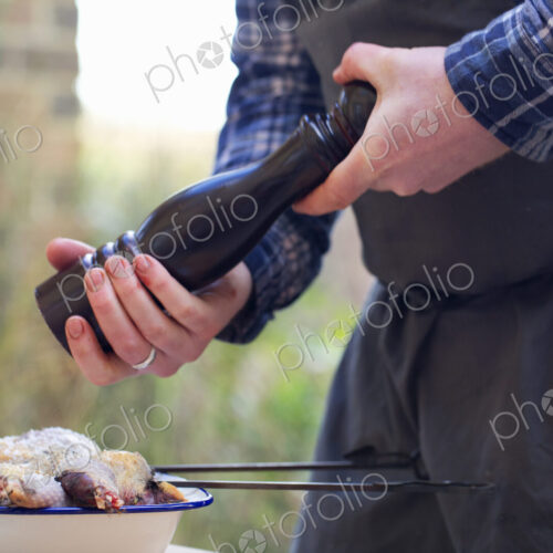 A spatchcocked game bird being seasoned for cooking, a man's hand grinding pepper in a… A spatchcocked game bird being seasoned for cooking, a man's hand grinding pepper in a…