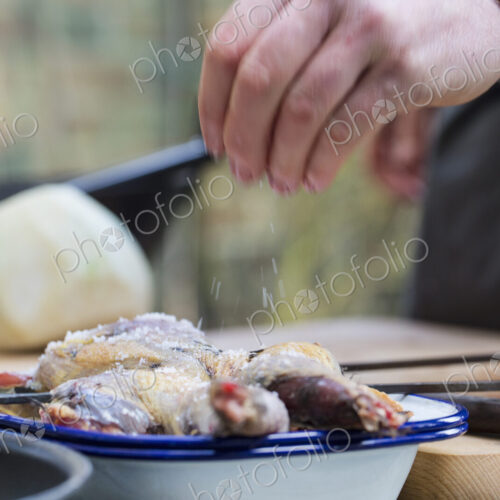 A spatchcocked game bird being seasoned for cooking, a man's hand sprinkling salt on… A spatchcocked game bird being seasoned for cooking, a man's hand sprinkling salt on…