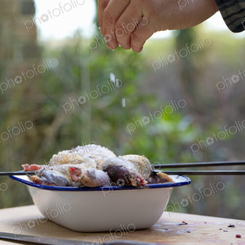 A spatchcocked game bird being seasoned for cooking, a man's hand sprinkling salt on… A spatchcocked game bird being seasoned for cooking, a man's hand sprinkling salt on…