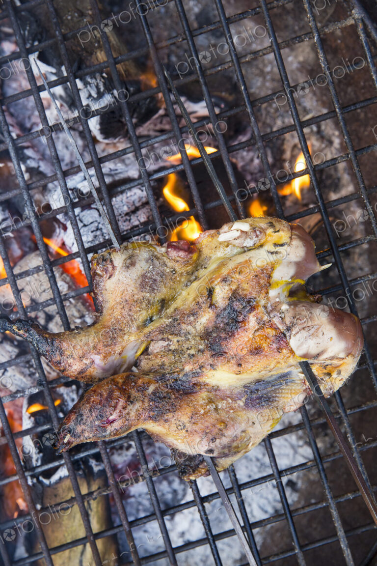 A spatchcocked game bird roasting above glowing coals.