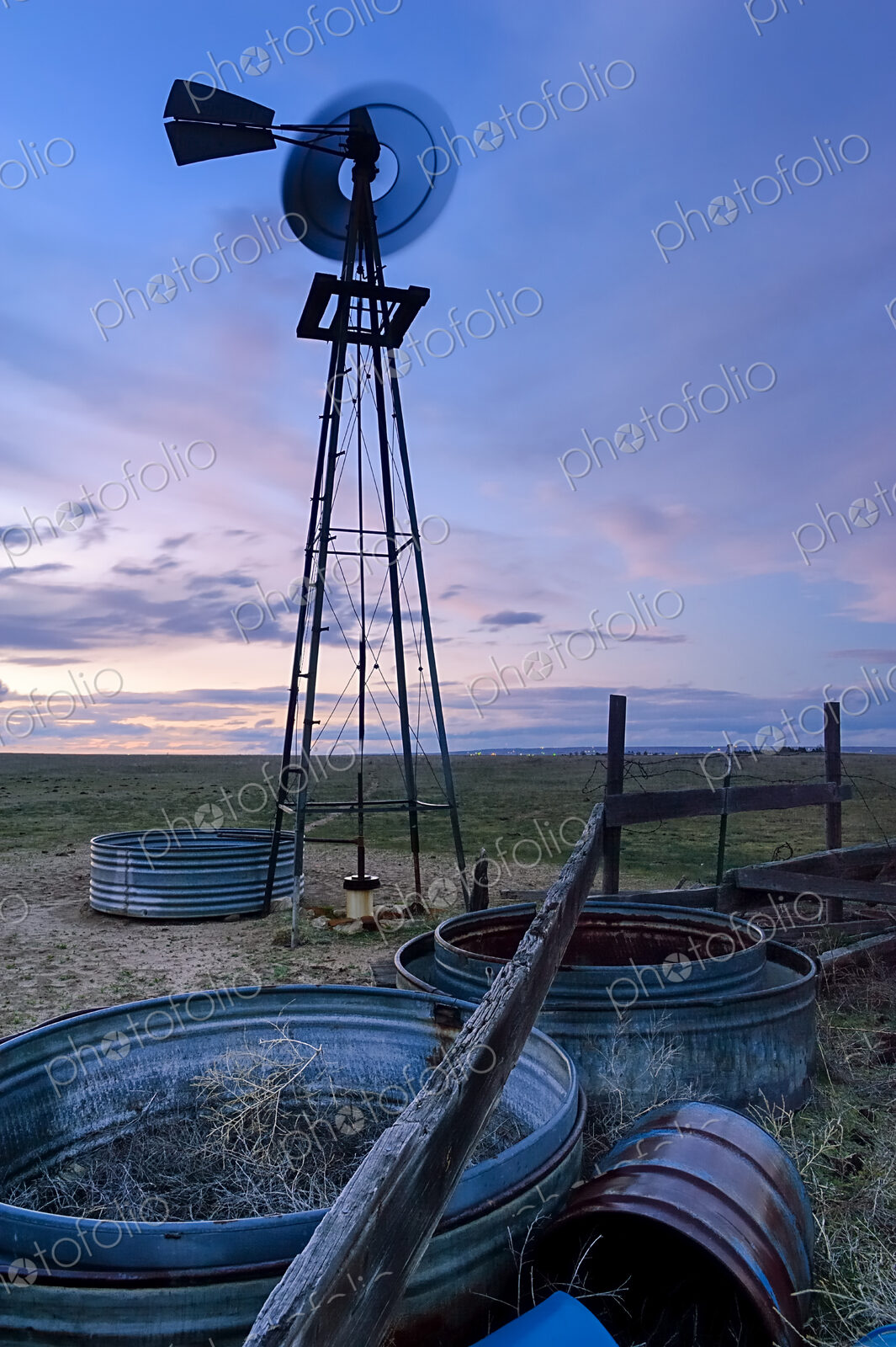 A spinning windmill metal wheel and wind tower, blurred motion, at sunset on the…