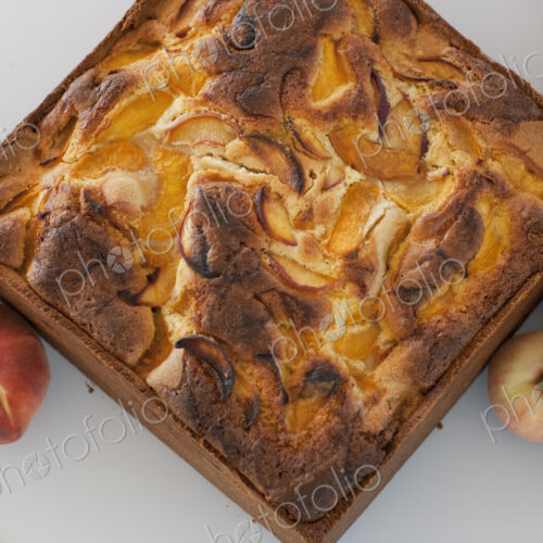 A square baked peach cake on a board with fresh peaches. Fruits. Organic fresh food on…