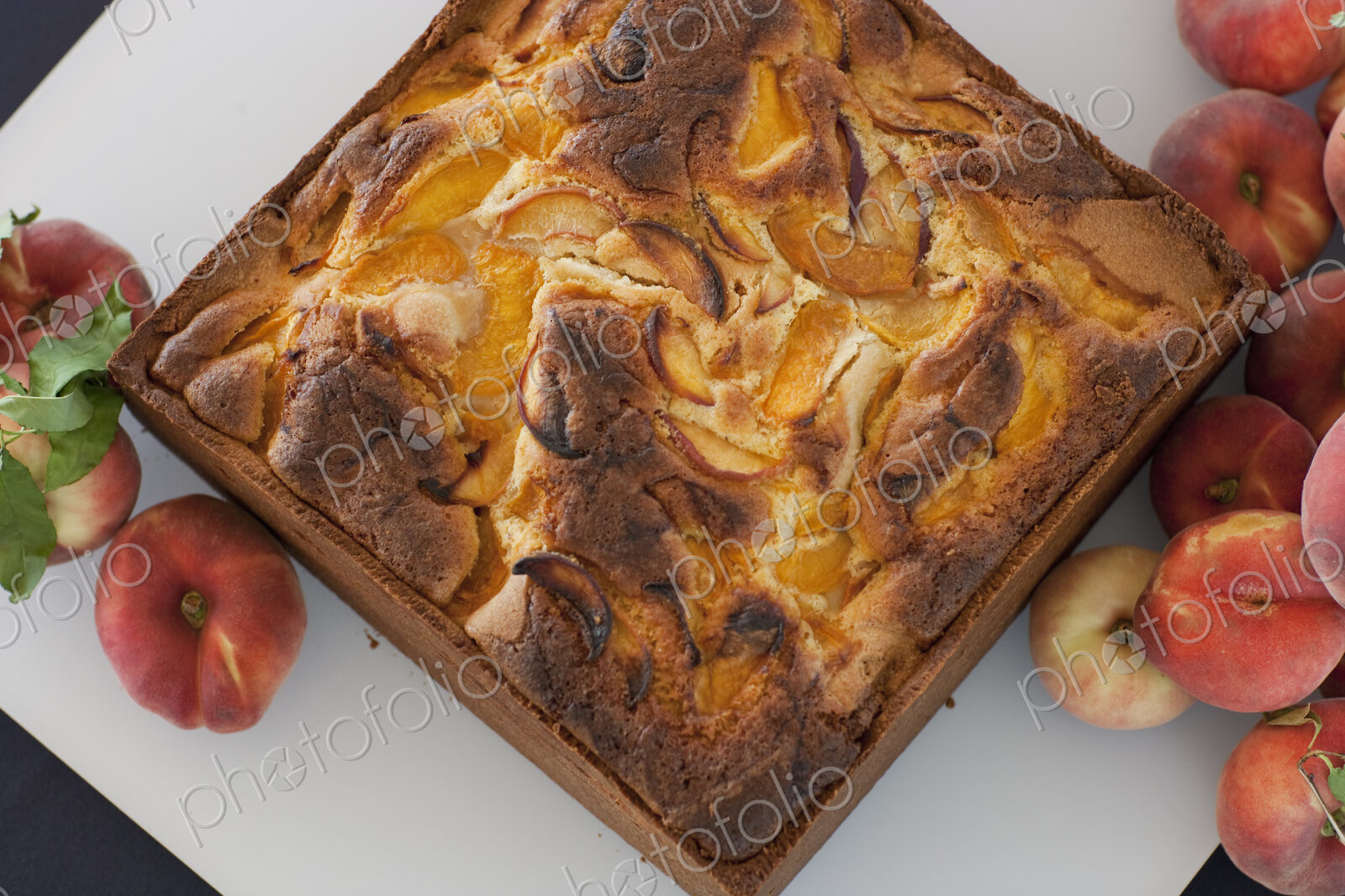 A square baked peach cake on a board with fresh peaches. Fruits. Organic fresh food on…