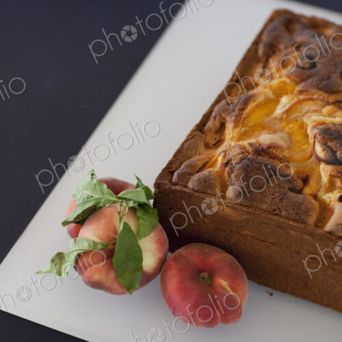 A square baked peach cake on a board with fresh peaches. Fruits. Organic fresh food on…