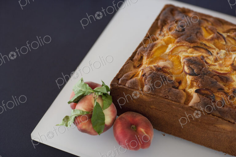 A square baked peach cake on a board with fresh peaches. Fruits. Organic fresh food on…