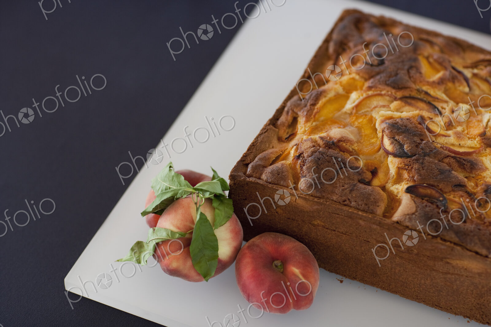 A square baked peach cake on a board with fresh peaches. Fruits. Organic fresh food on…