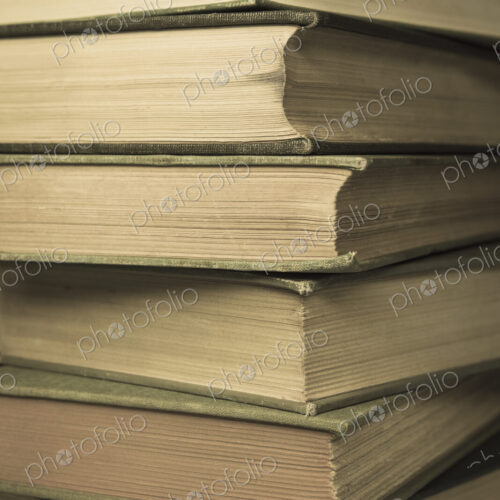 A stack of old hard cover books, with worn edges and aged yellowing paper.