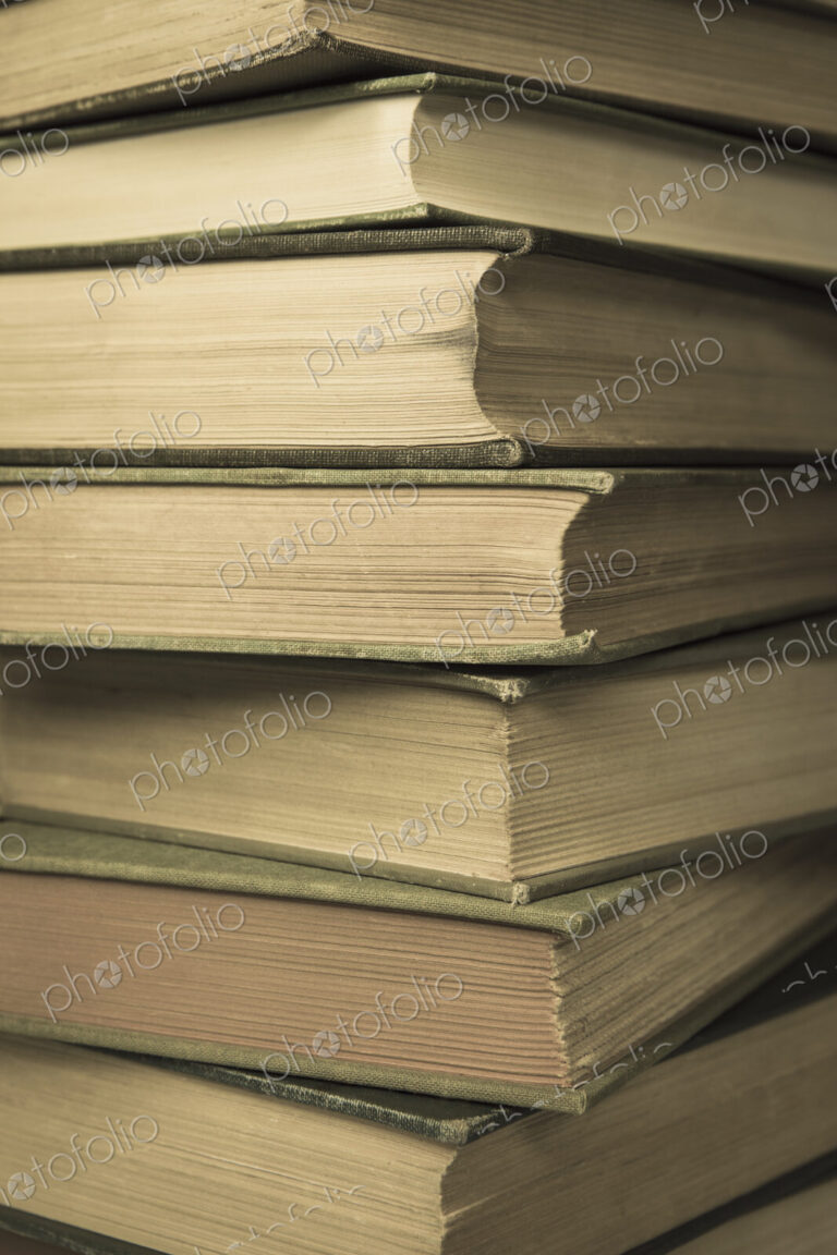 A stack of old hard cover books, with worn edges and aged yellowing paper.