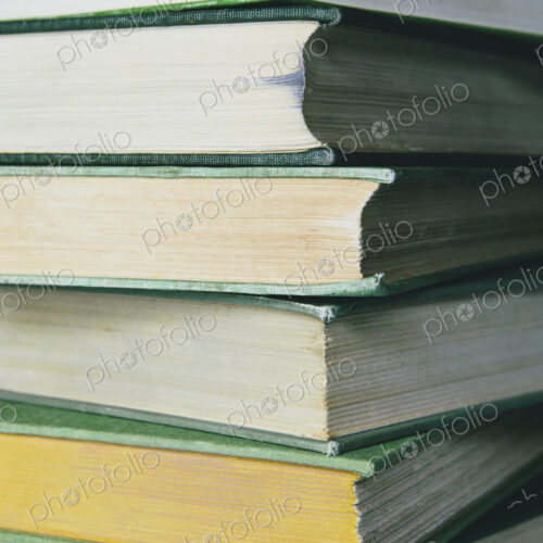 A stack of old hard cover books, with worn edges and paper that is stained or yellowed…