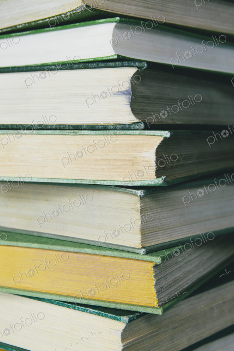 A stack of old hard cover books, with worn edges and paper that is stained or yellowed…