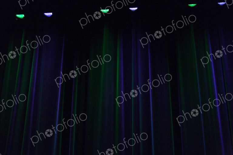 A stage in darkness,curtains and points of light, downlighters green and purple colours.