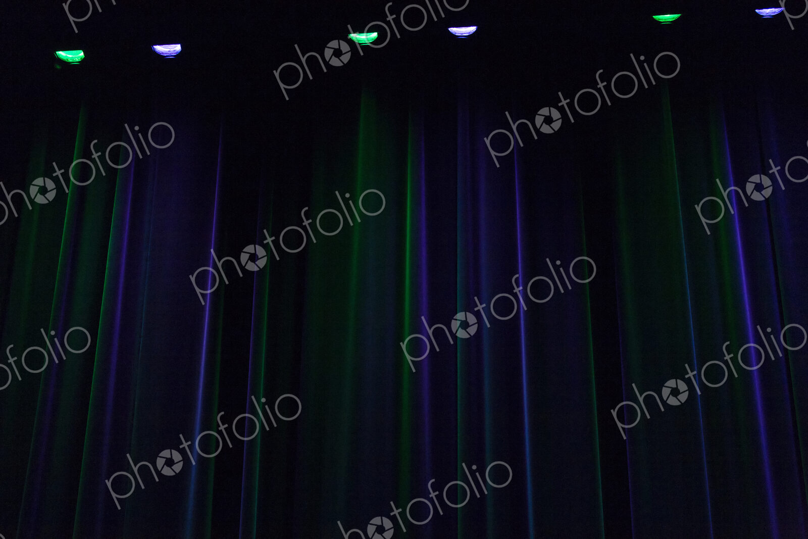 A stage in darkness,curtains and points of light, downlighters green and purple colours.