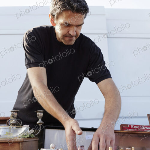 A stall holder arranging porcelain teapots at his stall at a flea market.