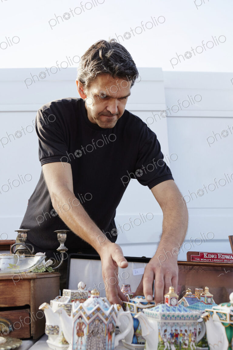 A stall holder arranging porcelain teapots at his stall at a flea market.