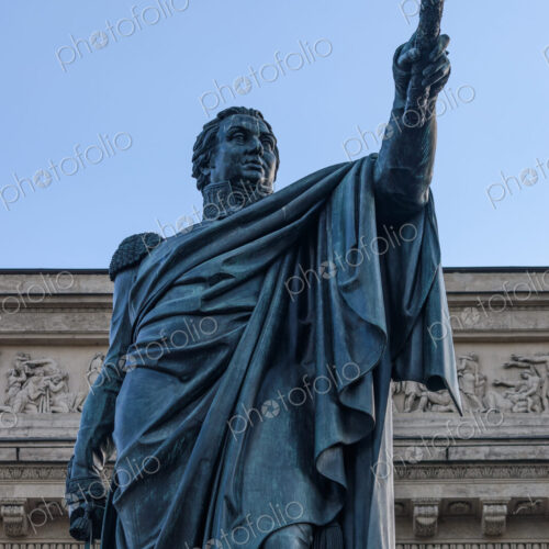 A statue of a classical figure, a man in a toga holding an arm up, outside a building. A statue of a classical figure, a man in a toga holding an arm up, outside a building.