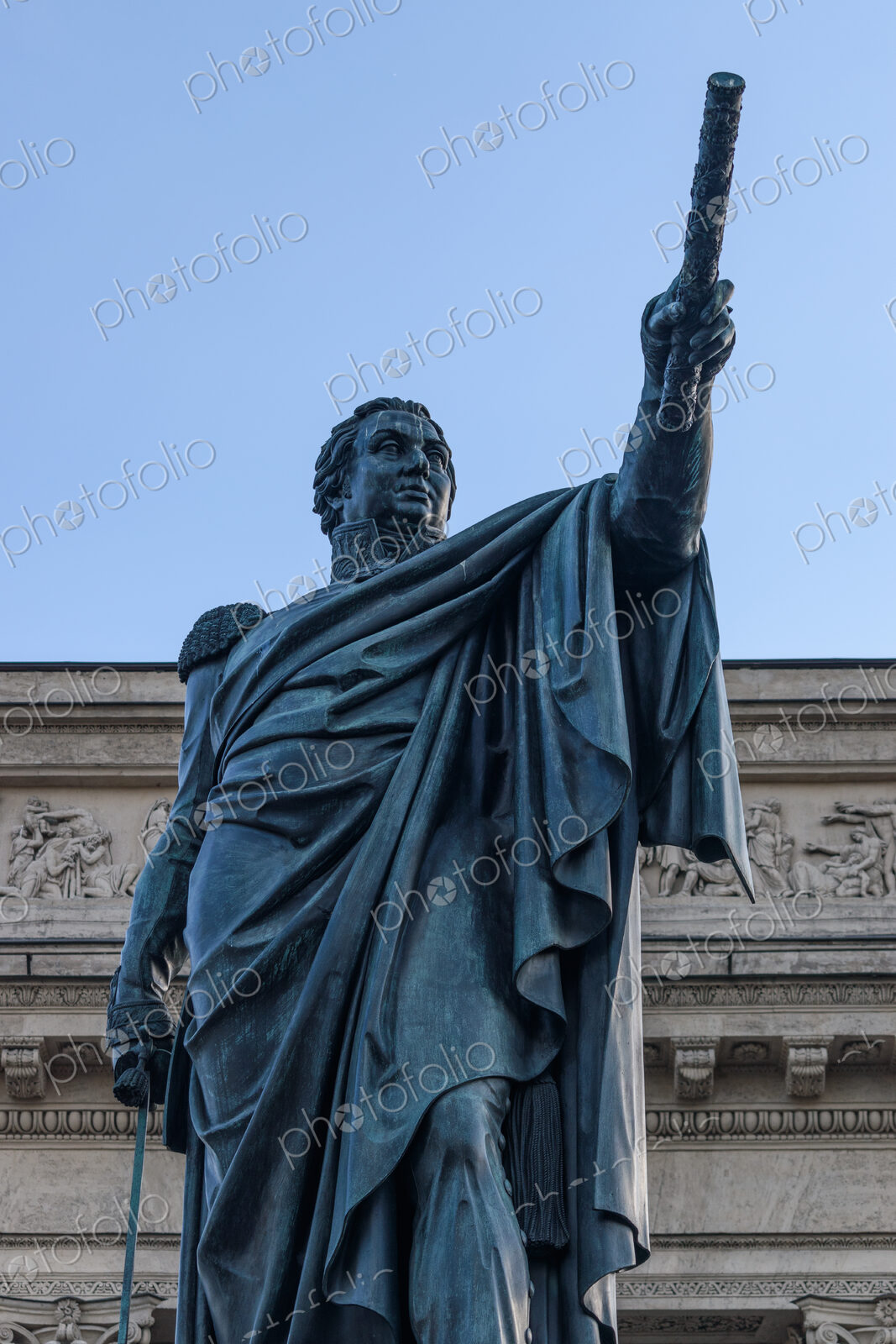 A statue of a classical figure, a man in a toga holding an arm up, outside a building.