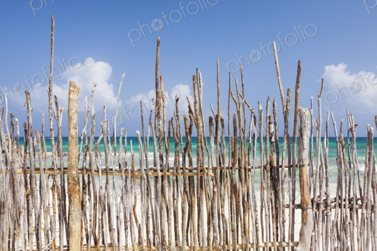 A stick fence along a white sand beach