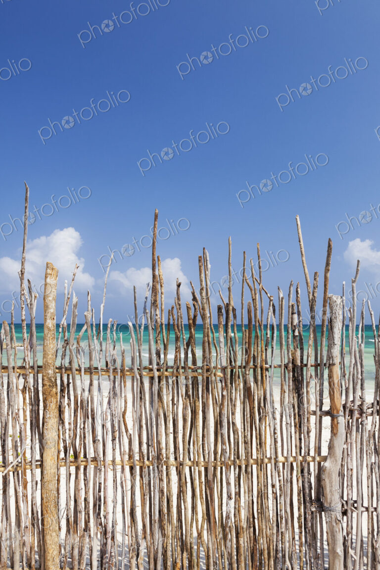 A stick fence along a white sand beach