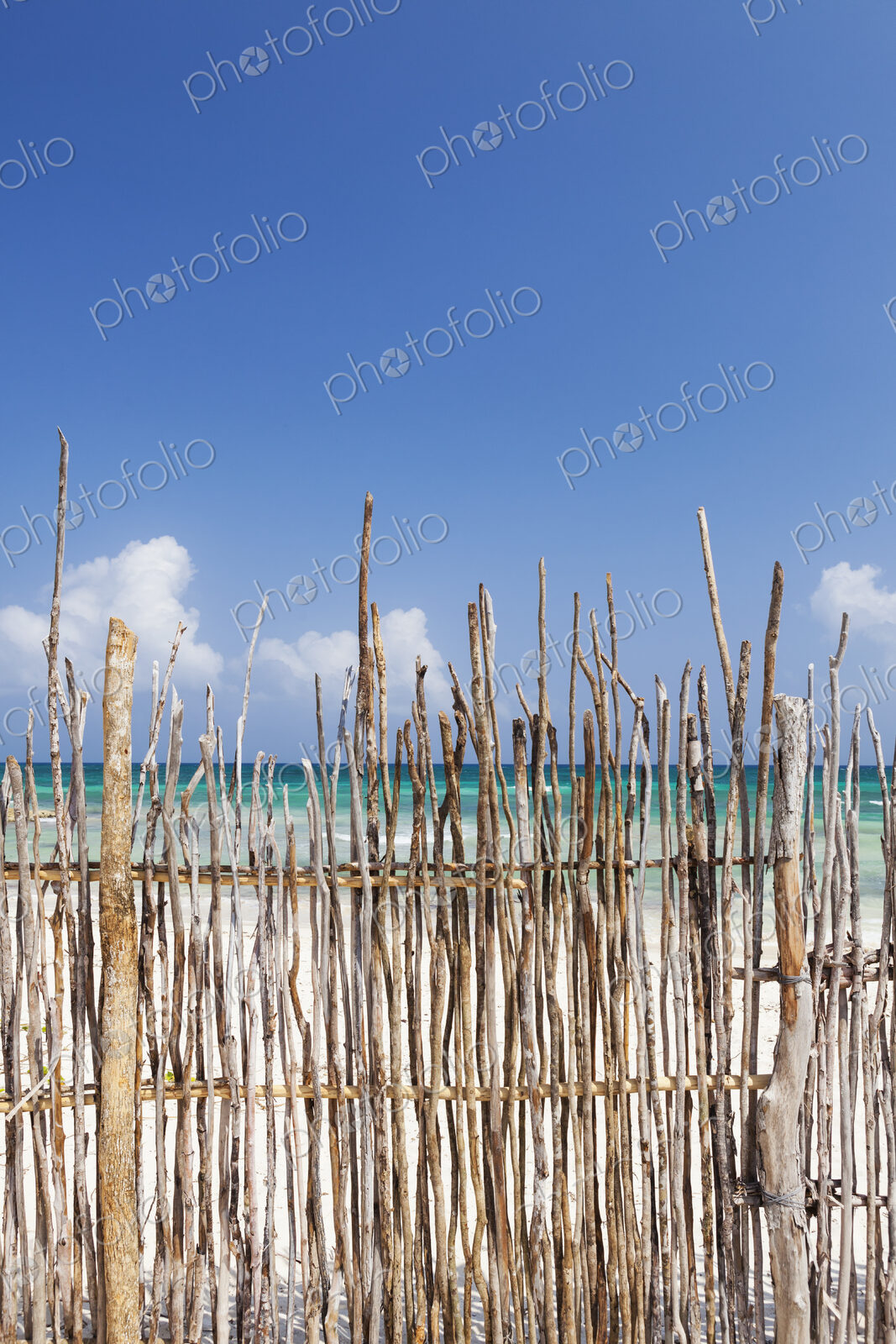 A stick fence along a white sand beach