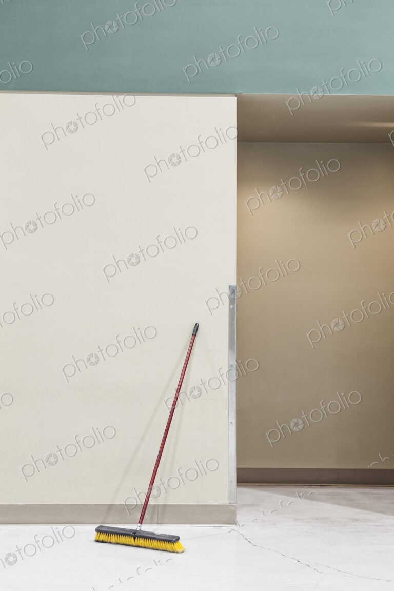 A still life view of a broom leaning up against a wall.