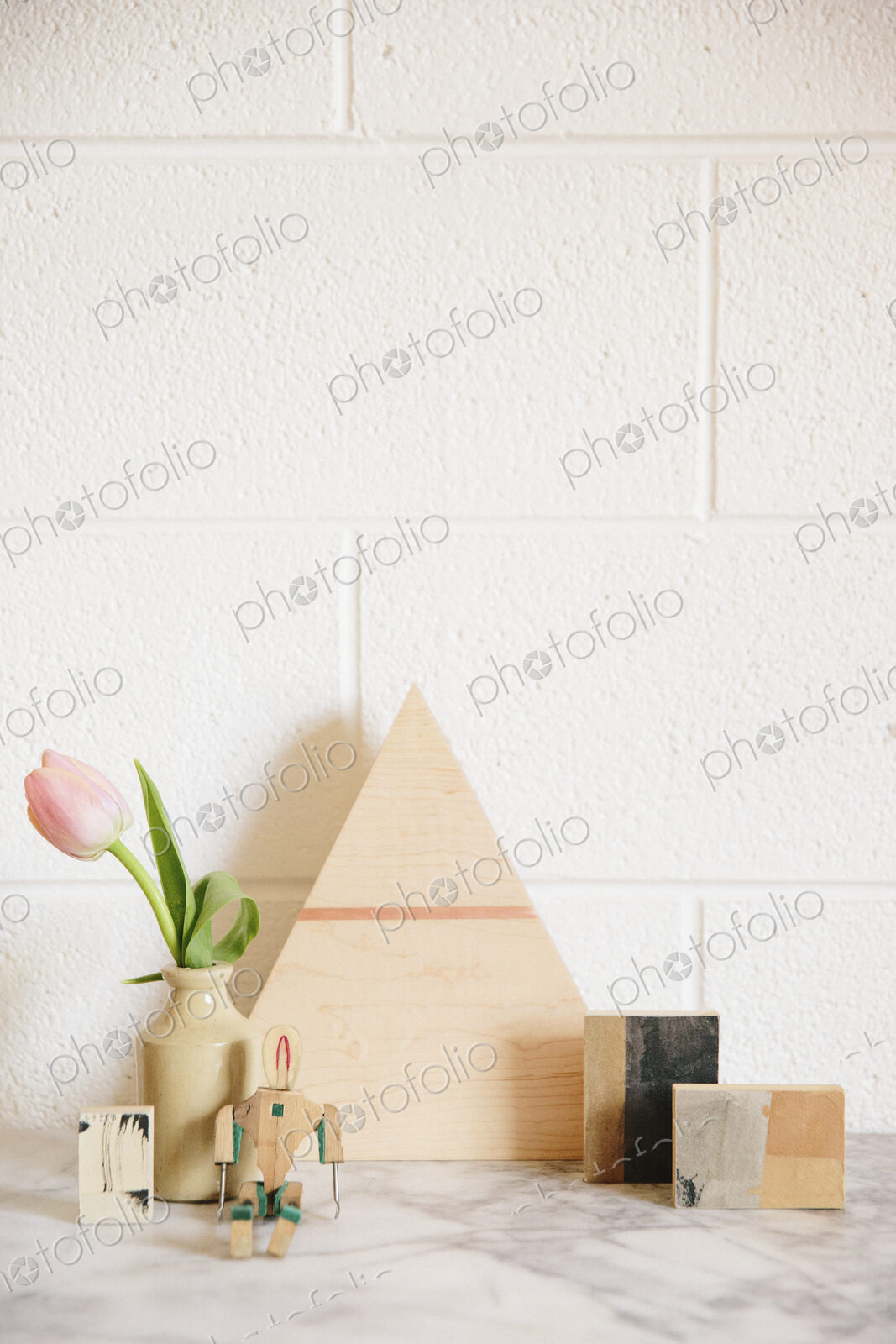A stone worktop with a wooden triangle of wood, small cubes of wood and a pink tulip…