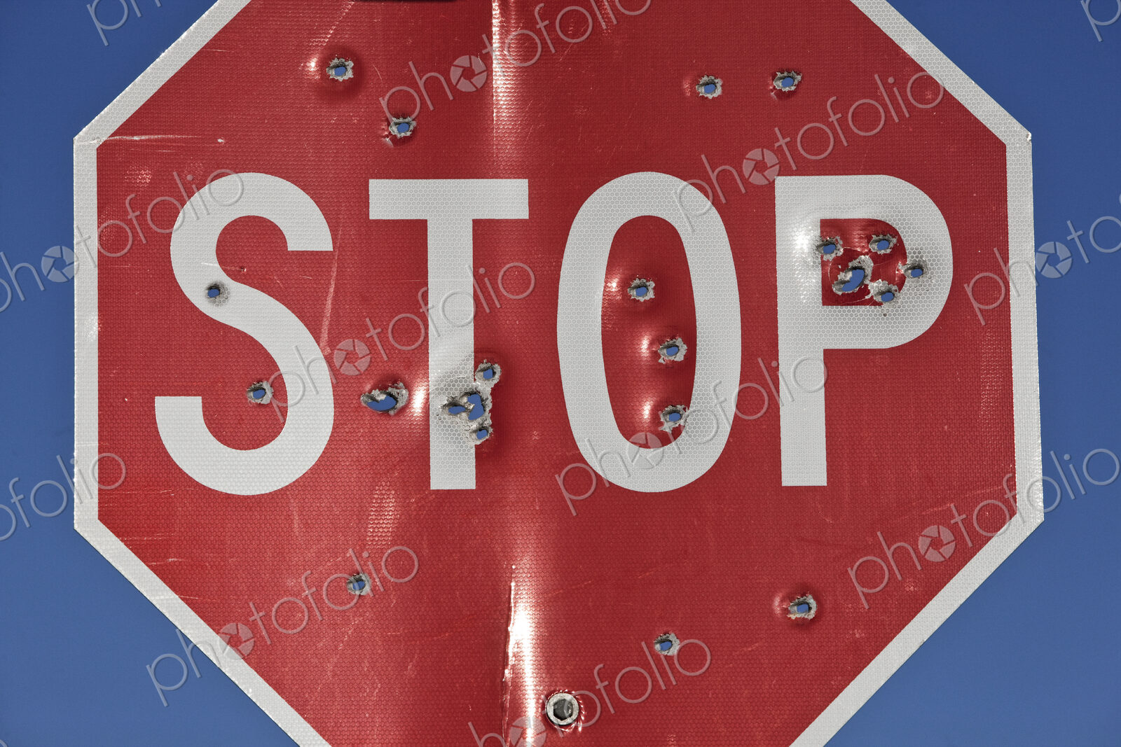 A stop sign that has been shot multiple times with a high powered rifle.