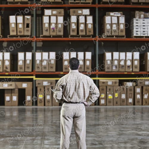 A storeroom manager looking at stock stacked high on shelves with his hand on his hip. A storeroom manager looking at stock stacked high on shelves with his hand on his hip.