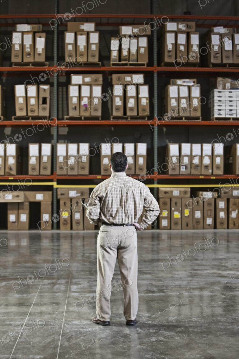 A storeroom manager looking at stock stacked high on shelves with his hand on his hip.