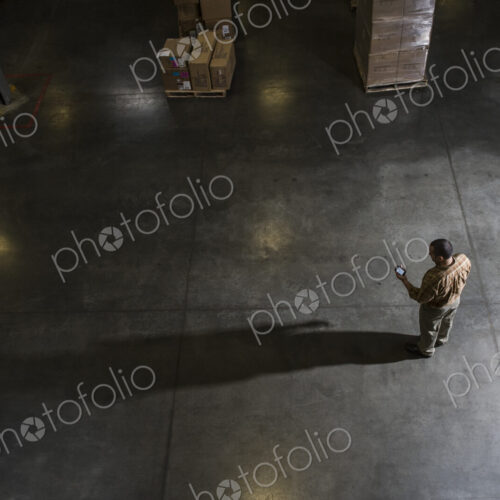 A storeroom manager seen from above in a darkened warehouse, looking at his phone.