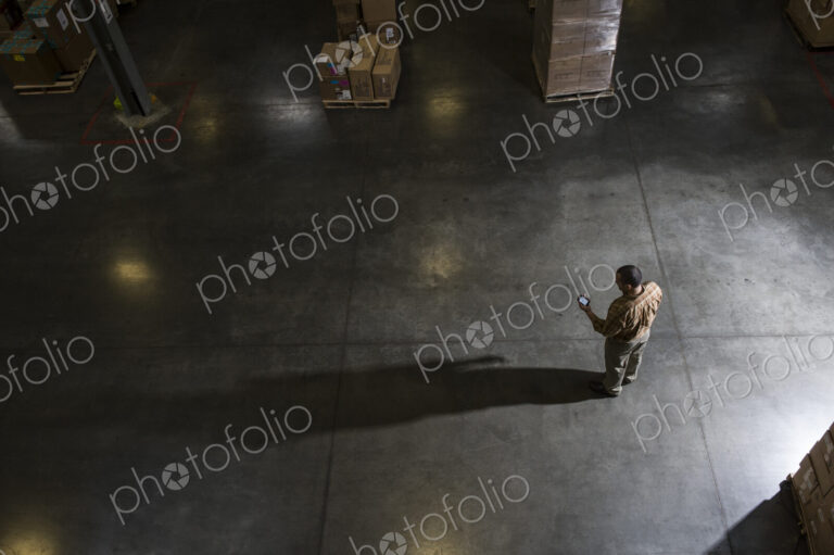 A storeroom manager seen from above in a darkened warehouse, looking at his phone.