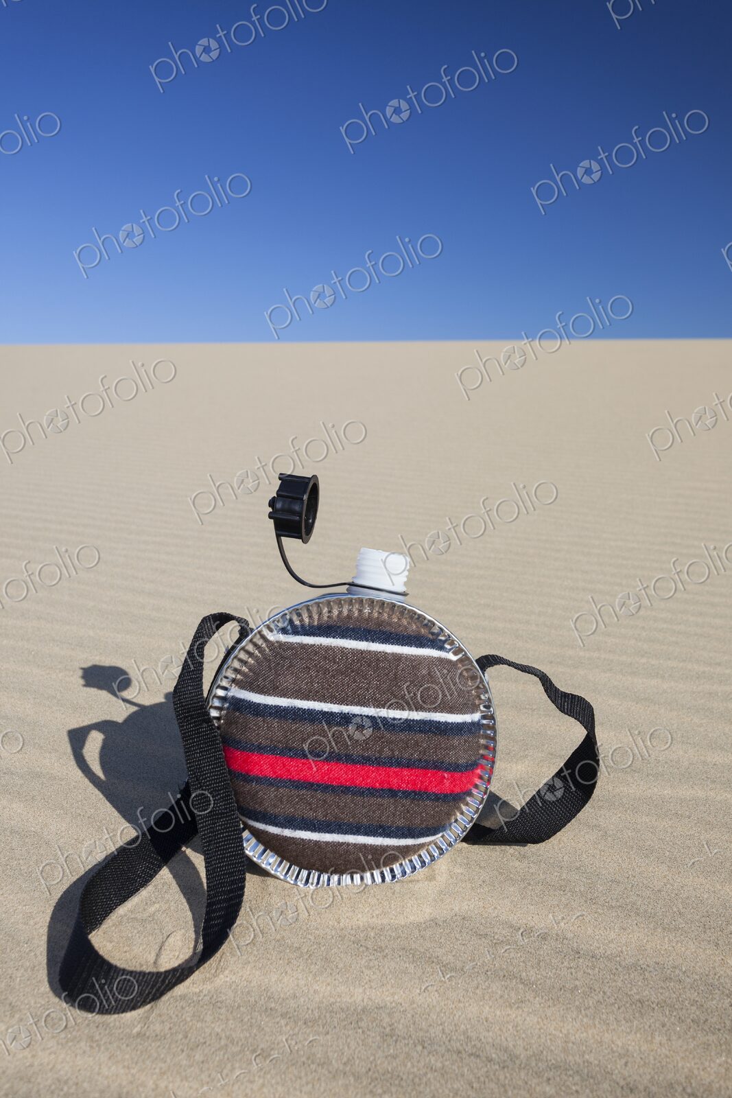 A striped fabric-covered canteen with a shoulder strap rests on the rippled surface of…