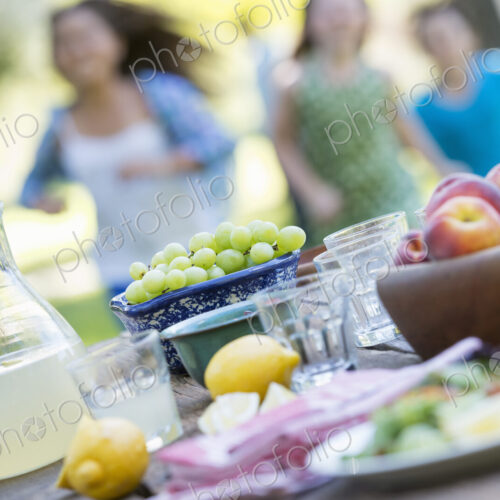 A summer buffet of fruits and vegetables, laid out on a table. Children running in the…